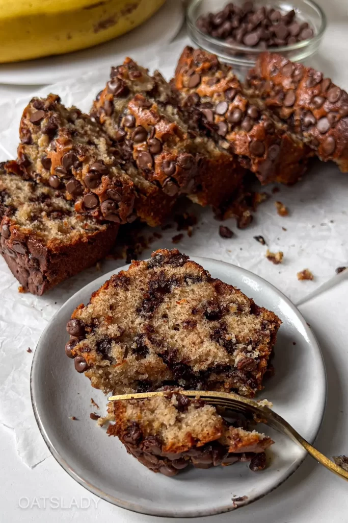 A sliced loaf of banana bread on a white plate showing the moist interior with chocolate chips