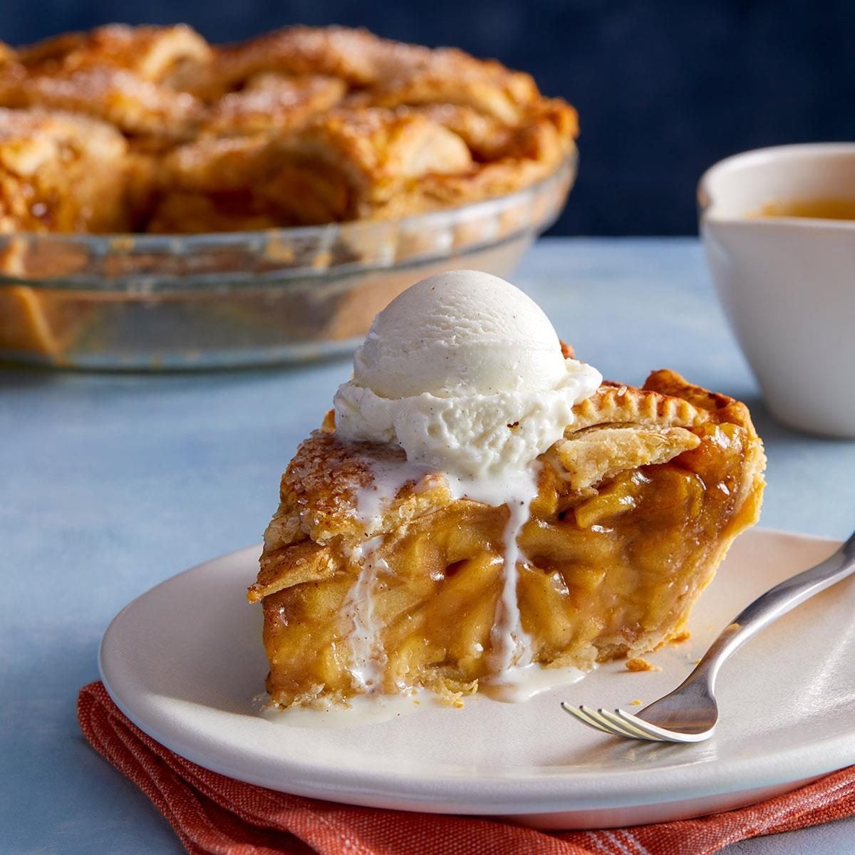 A slice of apple pie on a plate with a scoop of vanilla ice cream melting on top