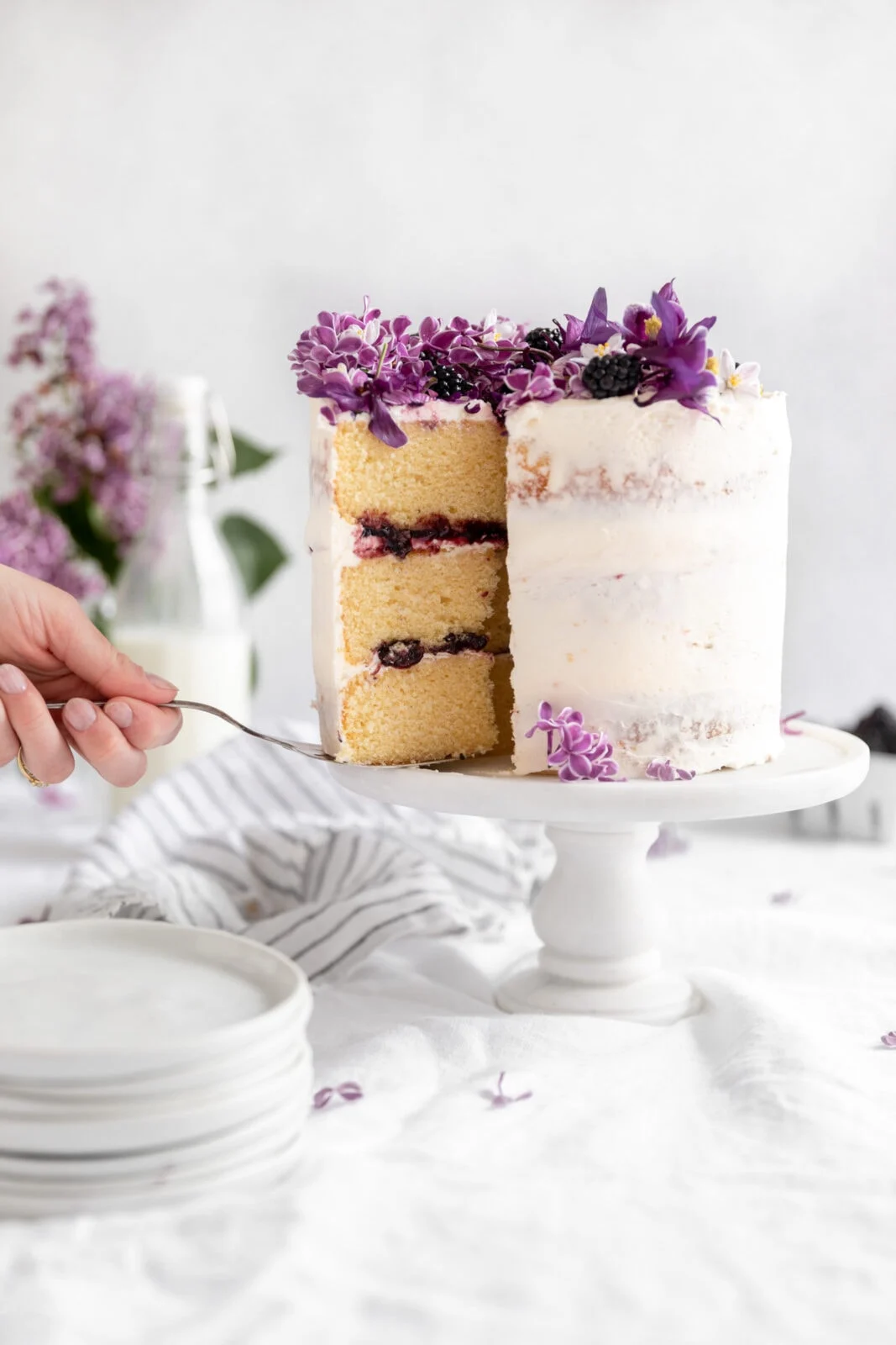 A three layer vanilla cake with white buttercream frosting and fresh flowers on top