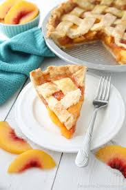 A slice of peach pie with lattice crust on a white plate with fresh peach slices beside it