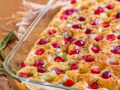 A loaf of rosemary focaccia in a pan topped with olive oil cherry tomatoes and fresh rosemary