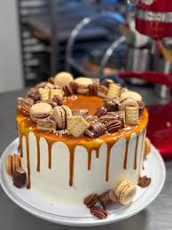 A chocolate drip cake on a cake stand with caramel dripping down the sides and topped with macarons